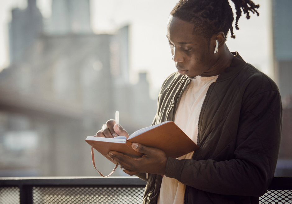 CFWA 2023 (1) A person is stood, looking at their notebook in deep though as they write a piece of creative non-fiction